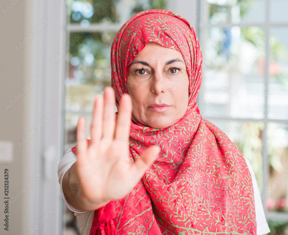 Middle aged muslim woman wearing hijab with open hand doing stop sign with serious and confident expression, defense gesture Middle aged muslim woman wearing hijab with open hand doing stop sign with serious and confident expression, defense gesture