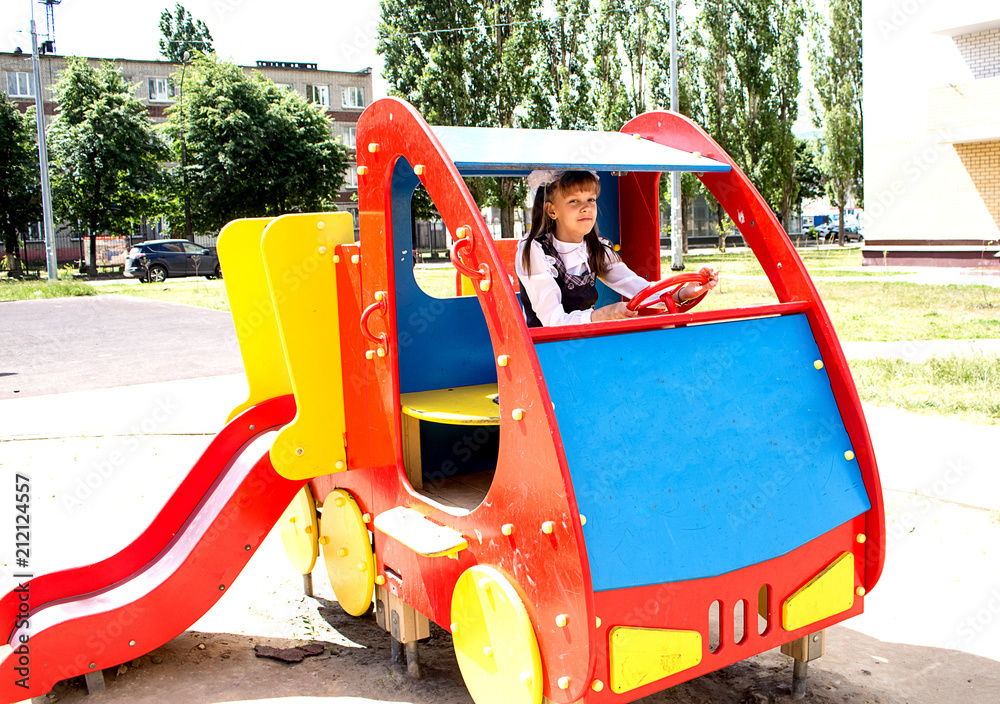 A teenage girl playing on the playground.  Sits at the wheel of a toy car.