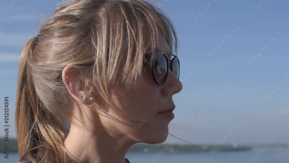 close-up portrait of a beautiful young girl in sunglasses against the blue sky and the sea. blond hair on a girls head in the wind