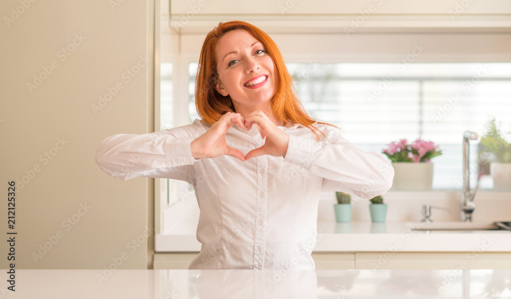 Redhead woman at kitchen smiling in love showing heart symbol and shape with hands. Romantic concept. Redhead woman at kitchen smiling in love showing heart symbol and shape with hands. Romantic concept.