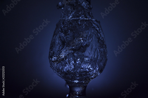 Simple still-life photo of whisky glass, water jet and dim colour light photo