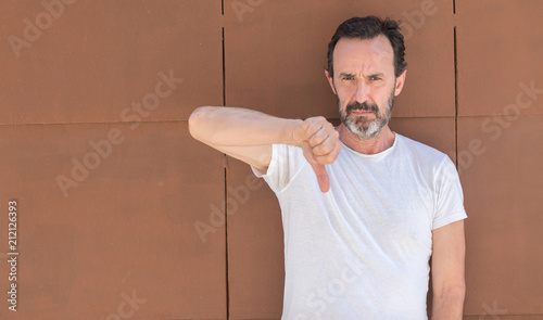 Handsome senior man standing over wall with angry face, negative sign showing dislike with thumbs down, rejection concept