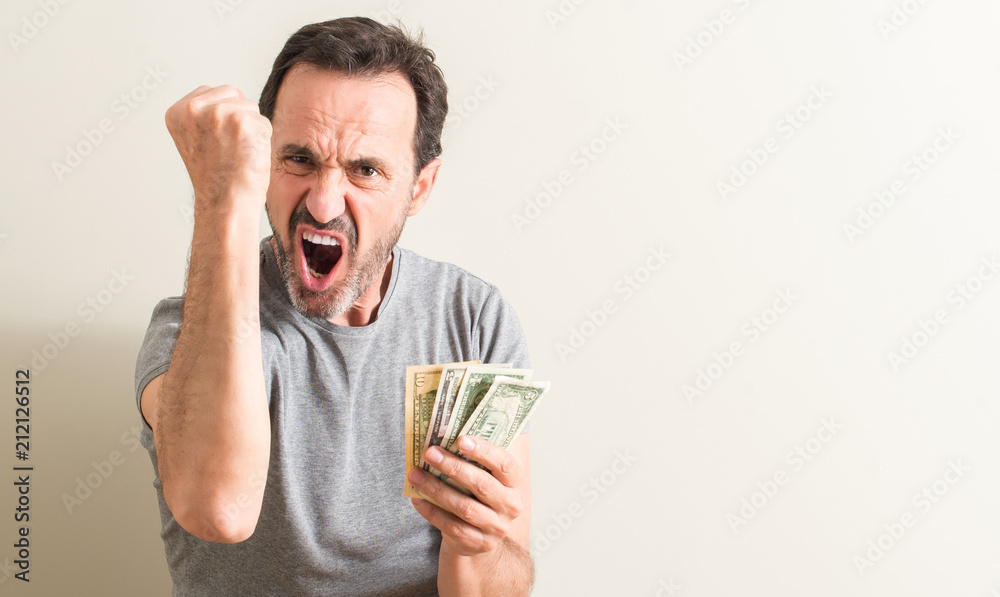 Senior man holding dollar money annoyed and frustrated shouting with anger, crazy and yelling with raised hand, anger concept Senior man holding dollar money annoyed and frustrated shouting with anger, crazy and yelling with raised hand, anger concept