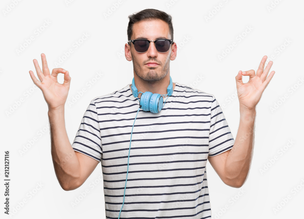 Naklejka premium Handsome young man wearing headphones relax and smiling with eyes closed doing meditation gesture with fingers. Yoga concept.