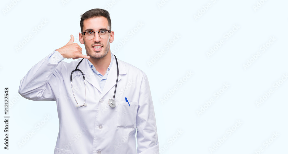 Handsome young doctor man smiling doing phone gesture with hand and fingers like talking on the telephone. Communicating concepts.