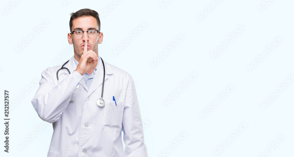 Handsome young doctor man asking to be quiet with finger on lips. Silence and secret concept.
