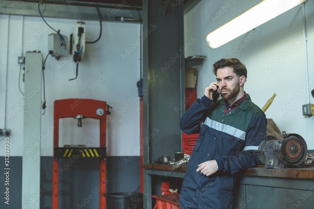 Mechanic talking on cell phone while standing in garage Mechanic talking on cell phone while standing in garage