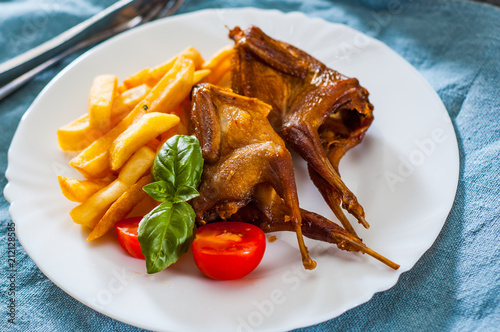 Roasted quails and potatoes served in a white plate on table photo