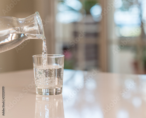 Closeup of bottle pouring watter in a glass on the table with sunny bokeh background at home.