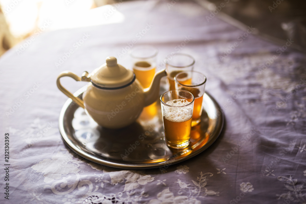 close up of a moroccan tea pot with glasses on a silver plate close up of a moroccan tea pot with glasses on a silver plate