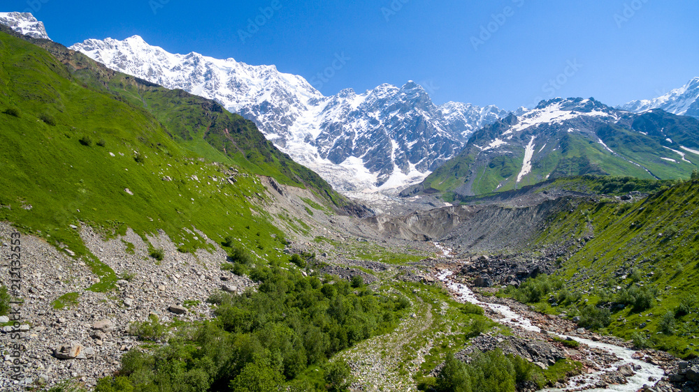 Glacier Shkhara, green slope and snow top of mountain aerial view