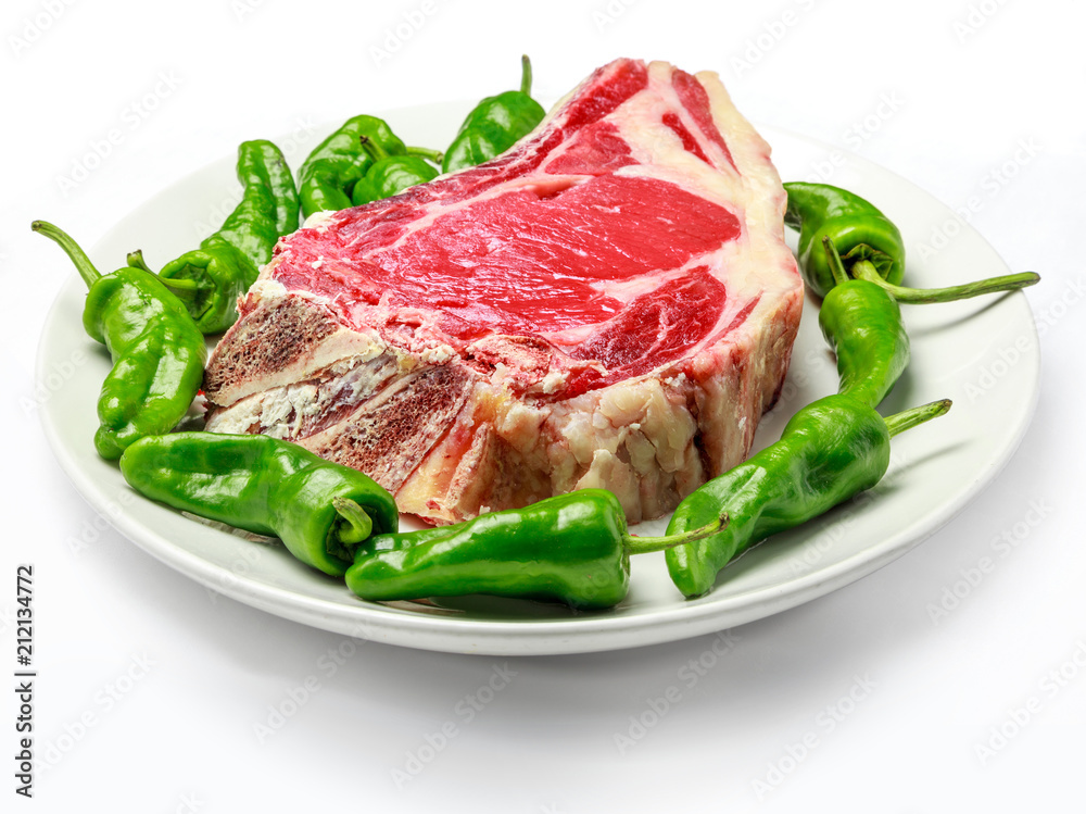 Great raw cutlet of cow with green peppers on plate and white backgrounds. High quality product, typical Spanish. Chuleton.