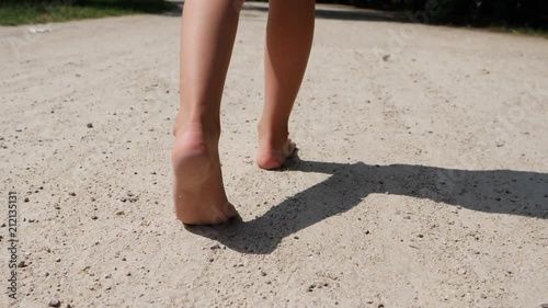 Child girl barefoot legs walk the ground park lane on hot summer day photo