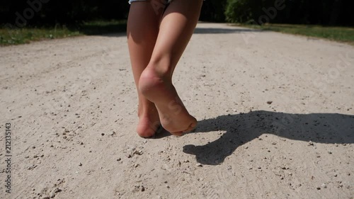 Child girl barefoot legs walk the ground park lane on hot summer day photo