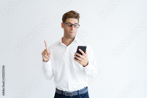 Portrait of serious businessman using phone showing idea gesture. Young Caucasian student searching for information with smartphone. Mobile technology concept