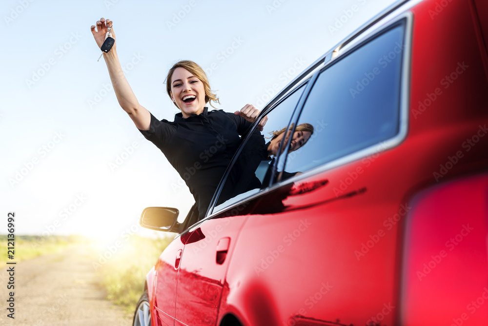 An attractive woman in the red car holds a car key in her hand.