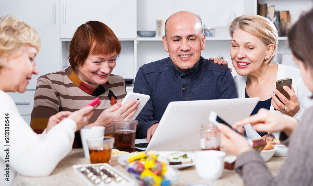 Fototapeta premium Smiling aged friends are sitting at table with notebook and talking about project