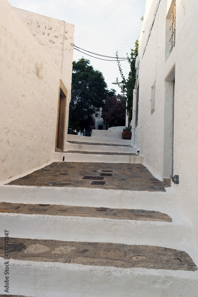 Naklejka premium A view of a narrow street with arch and wooden windows and doors with white wall stone architecture of the island Patmos, Greece