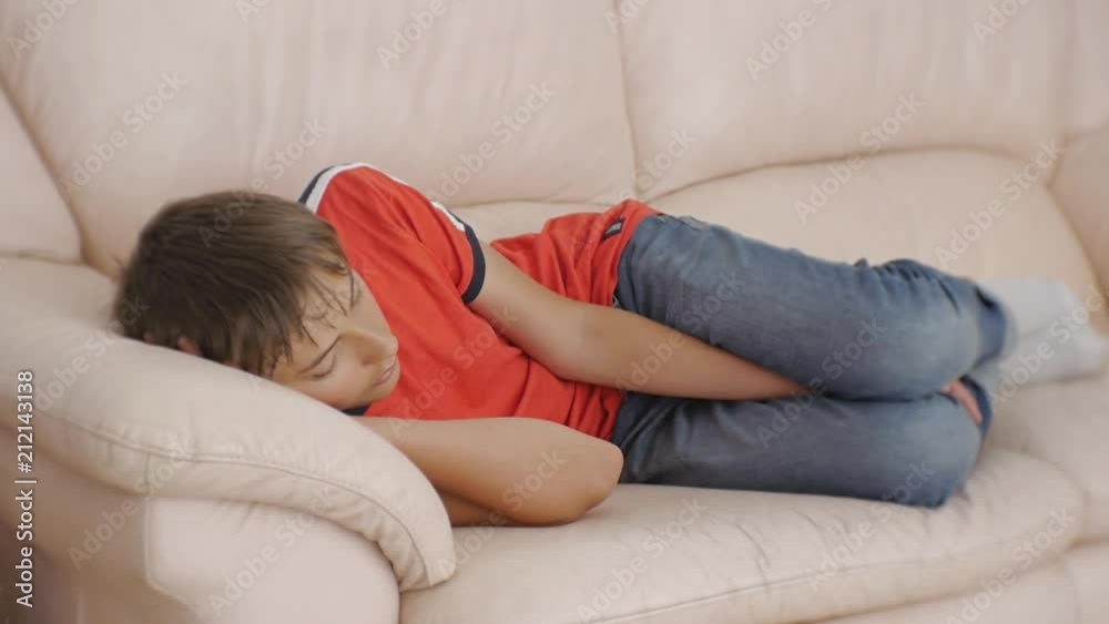Teenager sleeping on couch. Caucasian teen boy in red t-shirt and blue jeans sleeping on beige leather sofa in daytime. Lack of sleep Teenager sleeping on couch. Caucasian teen boy in red t-shirt and blue jeans sleeping on beige leather sofa in daytime. Lack of sleep