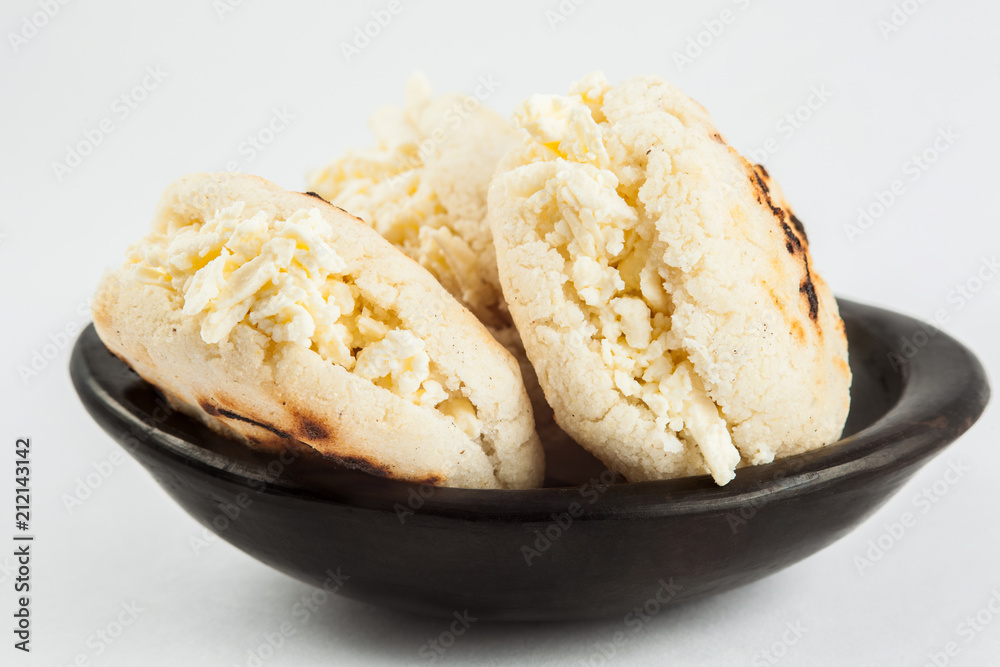 Colombian traditional white corn arepa stuffed with grated cheese in a black ceramic dish on black background Colombian traditional white corn arepa stuffed with grated cheese in a black ceramic dish on black background