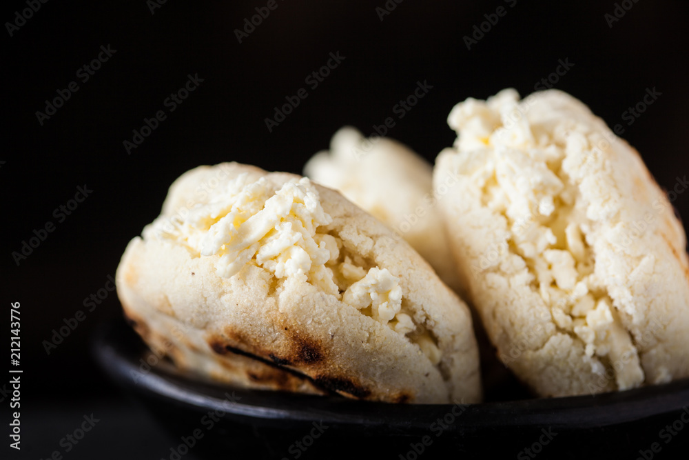 Colombian traditional white corn arepa stuffed with grated cheese in a black ceramic dish on black background Colombian traditional white corn arepa stuffed with grated cheese in a black ceramic dish on black background