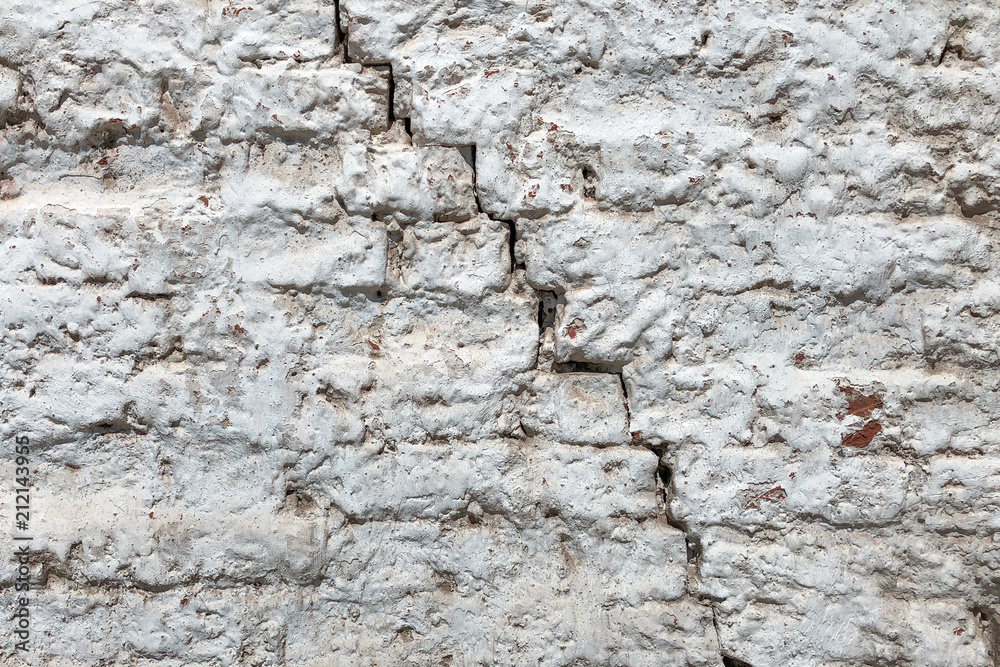 Old red brick wall covered with a white plaster and a large cracked. Texture background