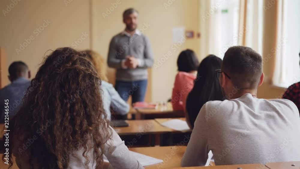High school students multiethnic class are listening to teacher, raising hands and asking questions while educator is explaining new information. Learning and teaching concept.