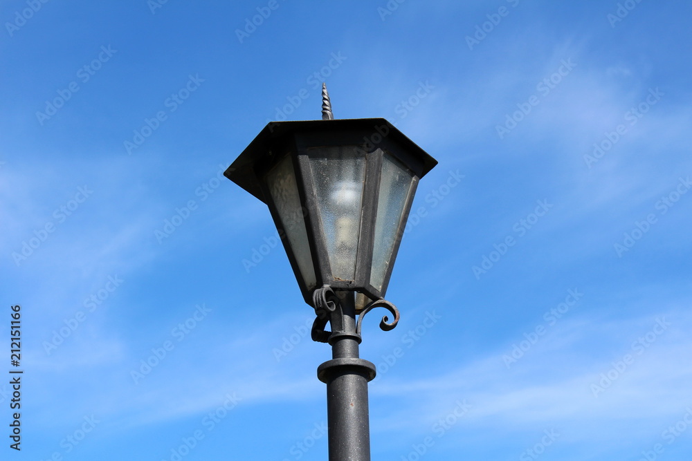 Antique baroque metal street lamp top with clear glass and LED light bulb inside on a sunny, but cloudy day Antique baroque metal street lamp top with clear glass and LED light bulb inside on a sunny, but cloudy day