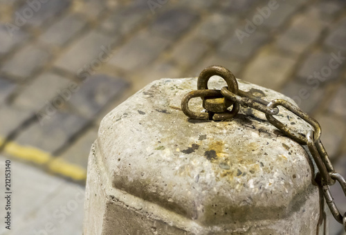 cement gray pedestal with an iron hook and part of the chain windblown on a blurred background road