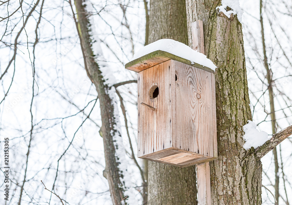 wooden birdhouse weathered covered with snow hanging on a tree trunk against the background of a winter sky wooden birdhouse weathered covered with snow hanging on a tree trunk against the background of a winter sky