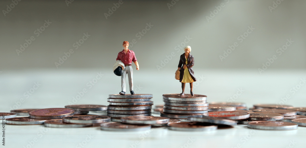 © Hyejin Kang - A miniature man and a miniature woman standing on top of a pile of coins of the same height.