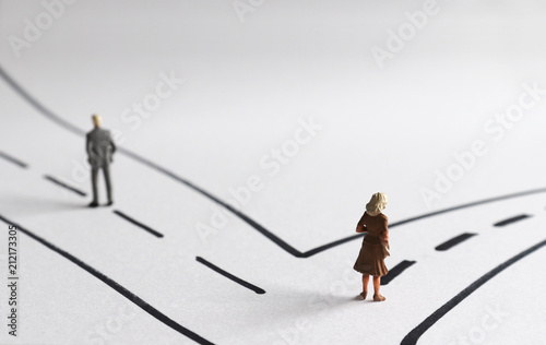 A miniature man and a miniature woman heading two different paths.