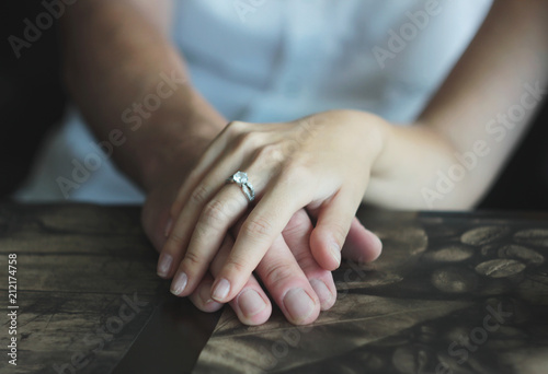 Woman's hand with an engagement ring on man's hand, date in the cafe