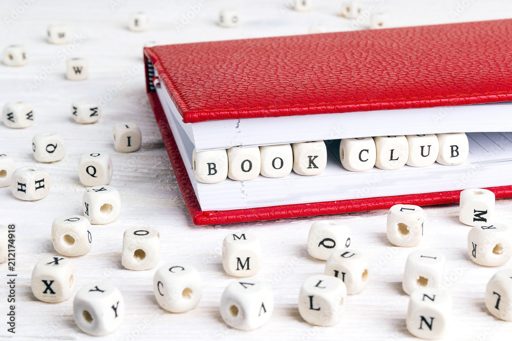 Obraz premium Phrase Book club written in wooden blocks in red notebook on white wooden table.