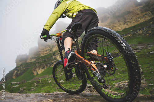 Legs of bicyclist and rear wheel close-up view of back mtb bike in mountains against background of rocks in foggy weather. The concept of extreme sports