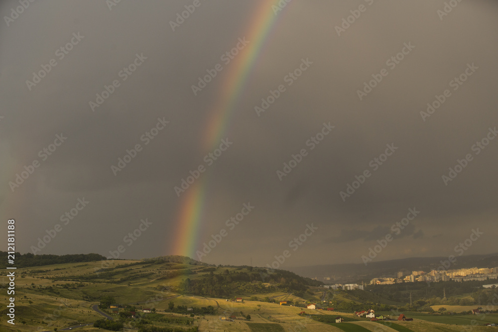 Beautiful rainbow over hills over the town and green hills