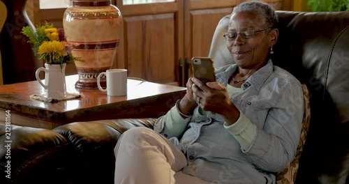 Happy smiling elderly black woman using her smart phone at home