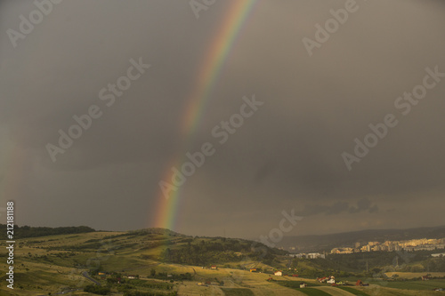 Beautiful rainbow over hills over the town and green hills