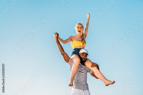 low angle view of happy young multiethnic couple having fun together against blue sky