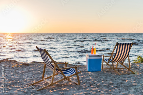 summer drinks on cooler and chaise lounges on sandy beach at sunset
