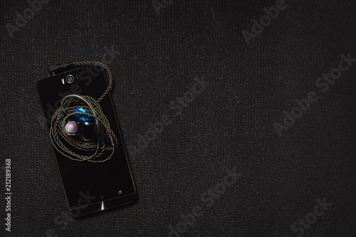 Top view smartphone with headphones on black background.