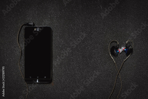 Top view smartphone with headphones on black background.