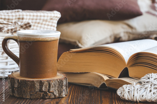 Details of still life in the home interior living room. Beautiful tea Cup, cut wood, books and pillows, candle on wooden background. Vintage, rustic. Cosy autumn-winter concept