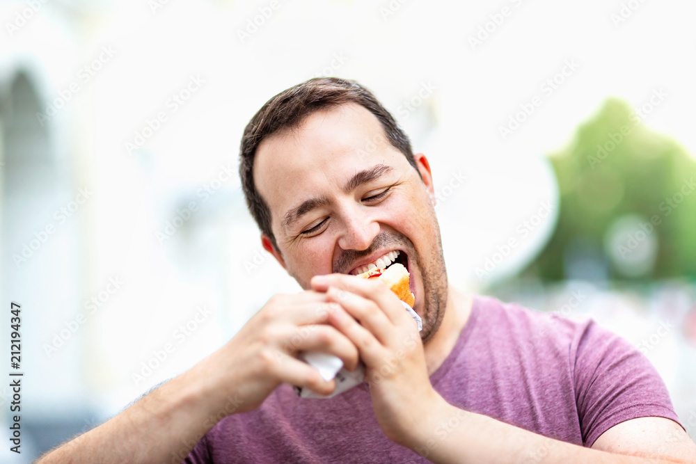 Closeup portrait of hungry man biting hot dog at city street background. Closeup portrait of hungry man biting hot dog at city street background.