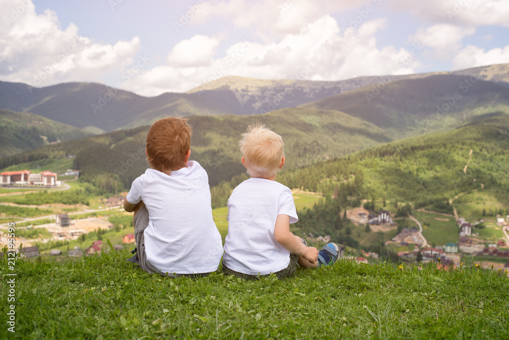 Two boys sitting on a hill and looking at the mountains. Back view Two boys sitting on a hill and looking at the mountains. Back view