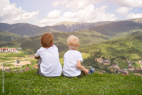 Two boys sitting on a hill and looking at the mountains. Back view