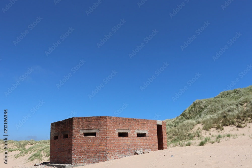 World War 2 anti-aircraft gun shelter on beach against blue sky with copy space