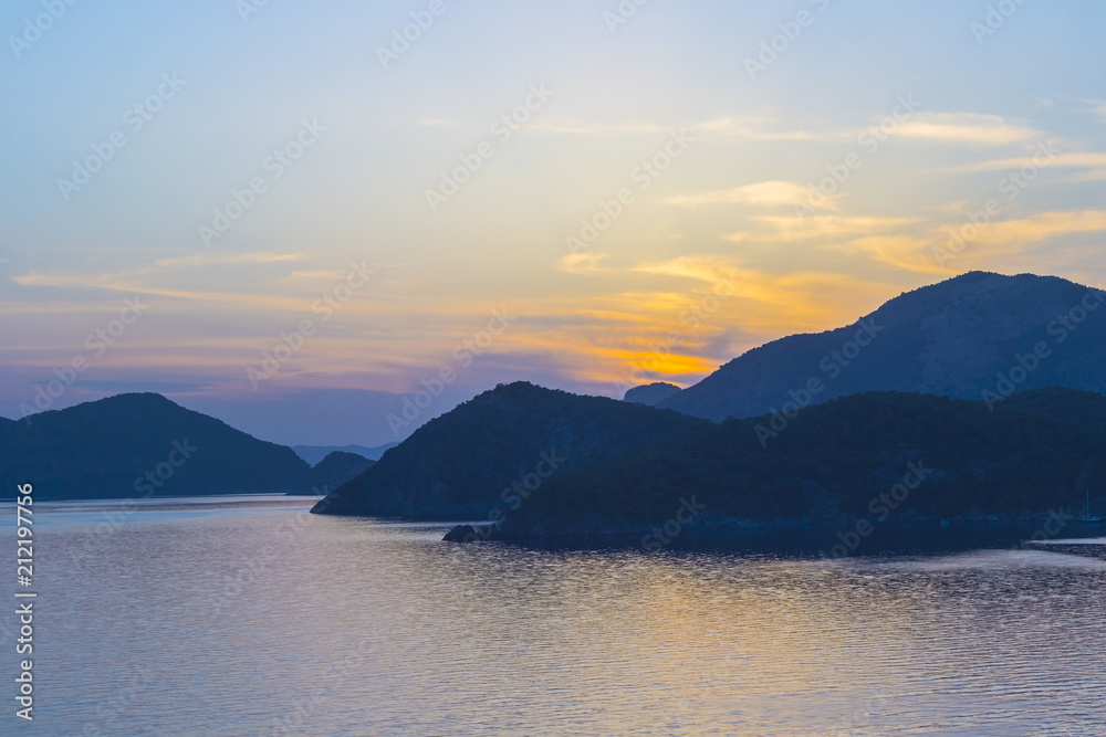 Mediterranean landscape. Sunset on the sea with flowing bright colored rays of the sun through the clouds. Silhouettes of mountains.  Background.