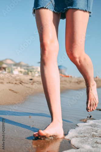 Young girl runs along the sea sandy beach barefoot, concept, legs.