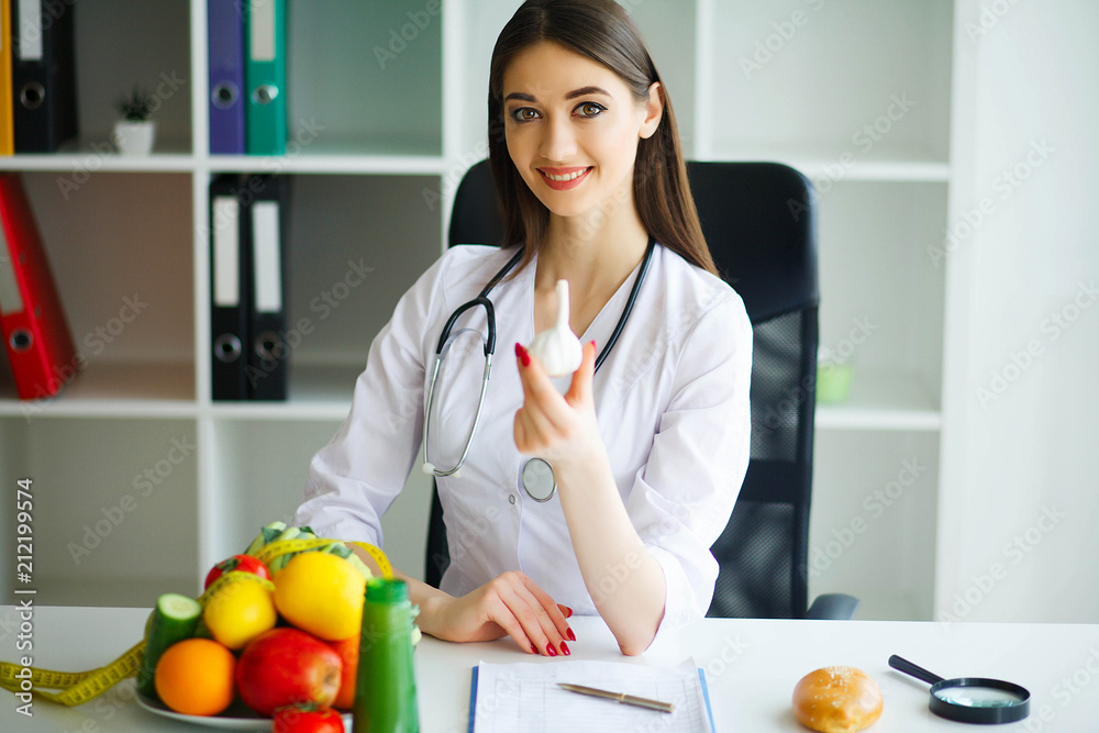 Health. The Doctor Dietitian Holds in the Hands of Garlic. Healthy Nutrition. Fresh Vegetables and Fruits on the Table. Happy Doctor in the Ligh Room. Health. The Doctor Dietitian Holds in the Hands of Garlic. Healthy Nutrition. Fresh Vegetables and Fruits on the Table. Happy Doctor in the Ligh Room.